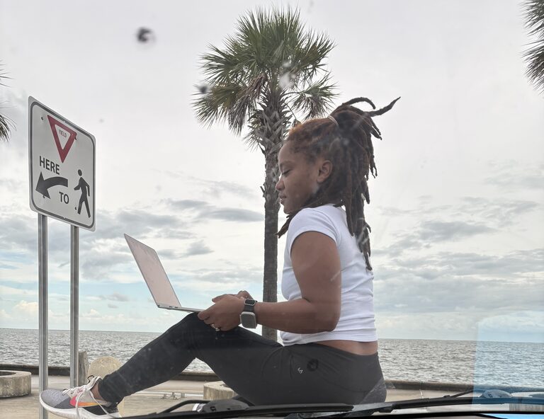 Ariel Deres working on a laptop outdoors by the water in New Orleans